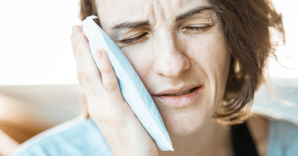 Woman holding a cold compress against her cheek with her eyes closed